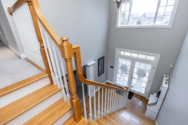 staircase featuring a towering ceiling, baseboards, wood finished floors, and french doors