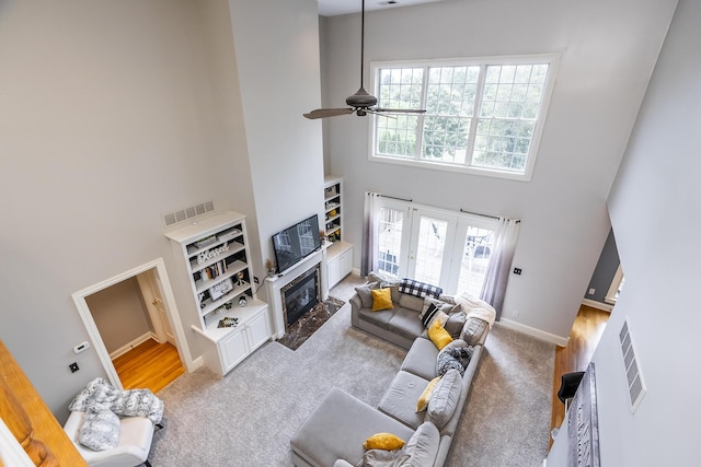 living area with visible vents, a high ceiling, a ceiling fan, a high end fireplace, and carpet flooring