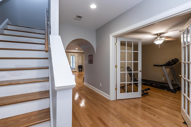 staircase featuring arched walkways, french doors, visible vents, and wood finished floors