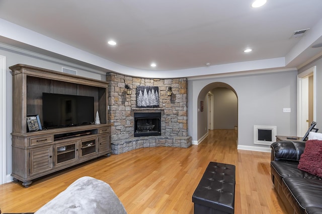 living room with arched walkways, a stone fireplace, light wood-style flooring, recessed lighting, and visible vents