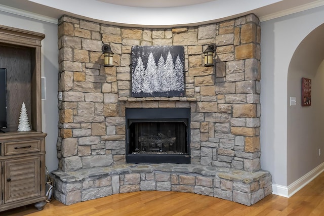 interior details featuring arched walkways, crown molding, a stone fireplace, and wood finished floors