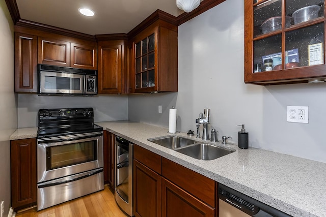 kitchen featuring stainless steel appliances, light wood finished floors, a sink, and glass insert cabinets