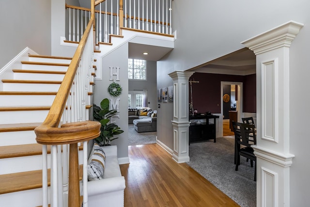 foyer entrance featuring wood finished floors, a towering ceiling, baseboards, stairway, and ornate columns