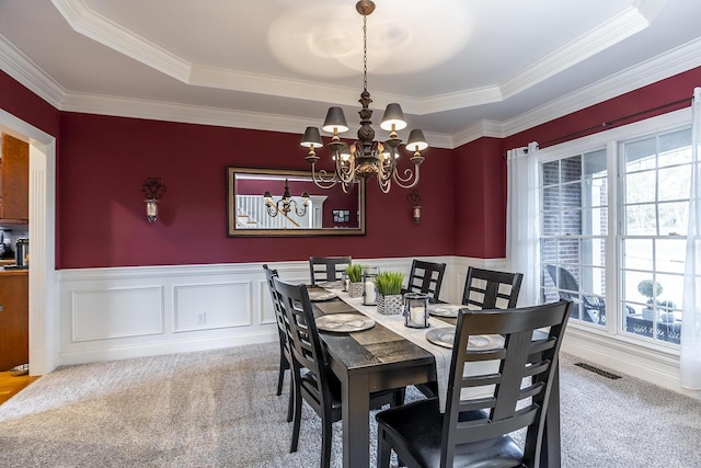 carpeted dining room with an inviting chandelier, visible vents, a tray ceiling, and wainscoting