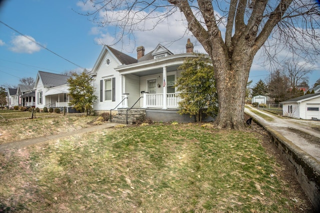 view of front facade with covered porch, a front lawn, and a chimney