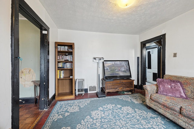 living room with a textured ceiling, visible vents, baseboards, parquet floors, and radiator