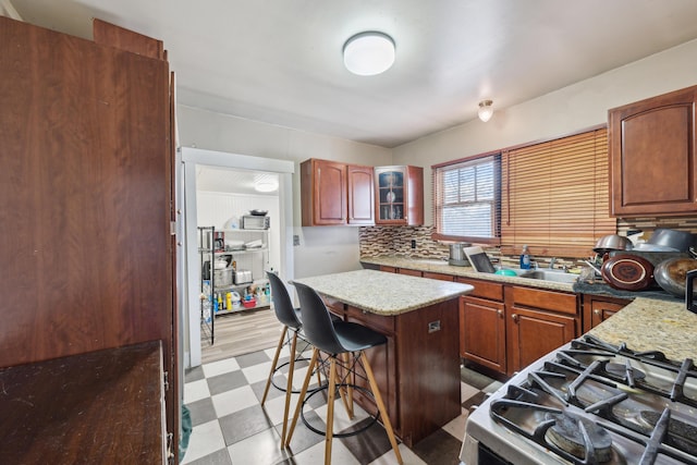 kitchen with range with gas stovetop, a center island, light floors, tasteful backsplash, and glass insert cabinets