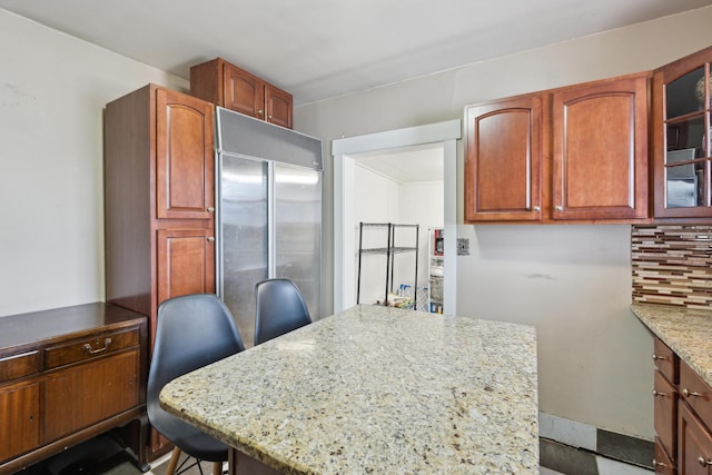 kitchen with tasteful backsplash, glass insert cabinets, a kitchen island, light stone countertops, and built in refrigerator