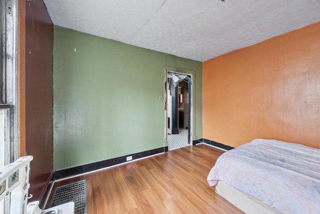 bedroom with a textured ceiling, wood finished floors, and baseboards