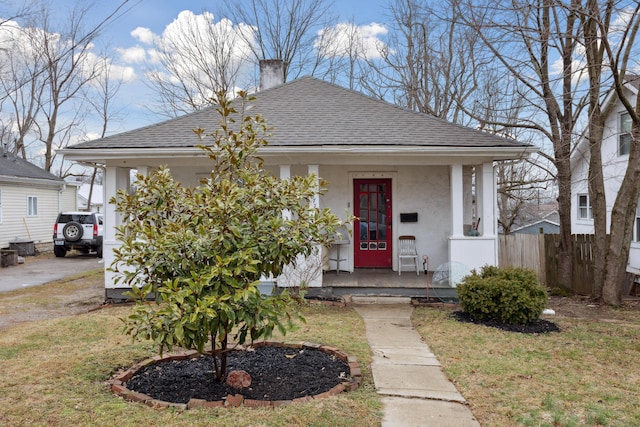 view of front facade featuring a chimney, roof with shingles, fence, a porch, and stucco siding