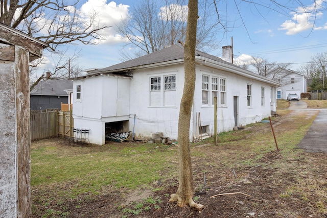 view of side of home with a shingled roof, a chimney, and fence