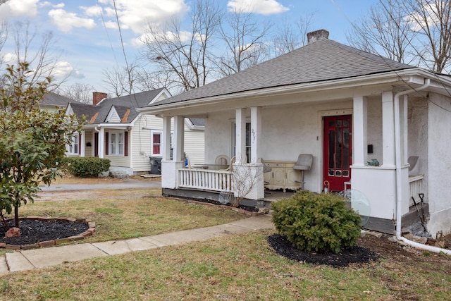 view of front of house with a porch, roof with shingles, stucco siding, a front lawn, and a chimney