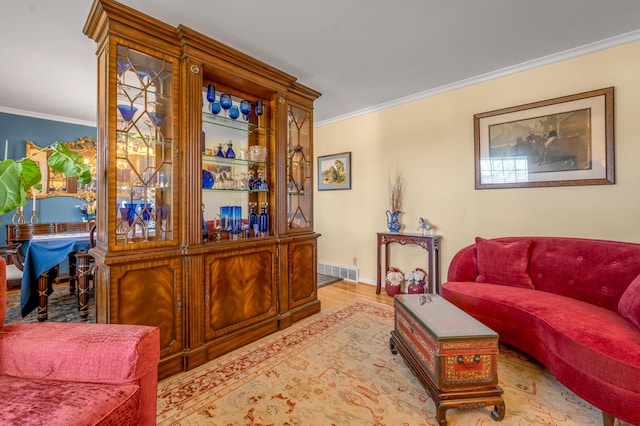 living area with baseboards, wood finished floors, visible vents, and crown molding