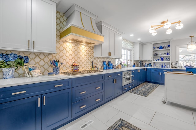 kitchen featuring blue cabinets, stainless steel appliances, a sink, open shelves, and custom range hood