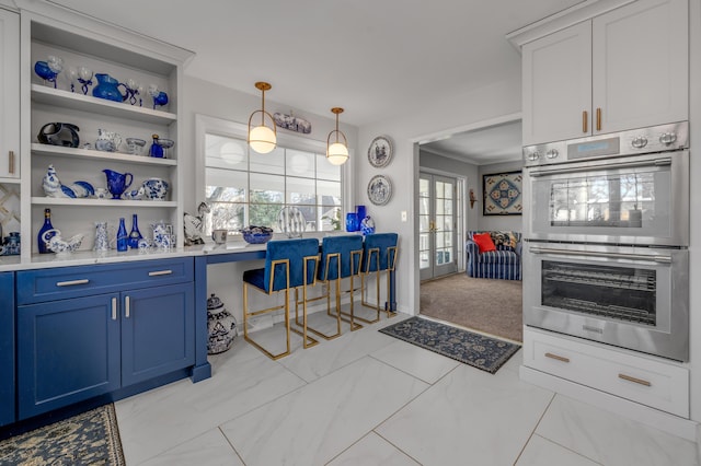 kitchen with double oven, blue cabinets, marble finish floor, open shelves, and decorative light fixtures