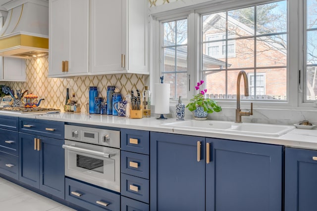 kitchen featuring blue cabinetry, custom range hood, a sink, and oven