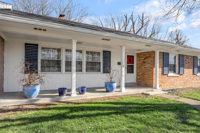 property entrance featuring a chimney, brick siding, a lawn, and a porch