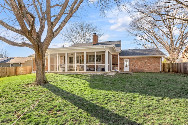 rear view of house with brick siding, a chimney, a lawn, a sunroom, and a fenced backyard