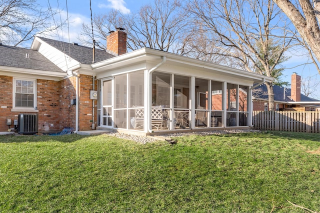 back of property featuring brick siding, fence, a sunroom, a lawn, and a chimney