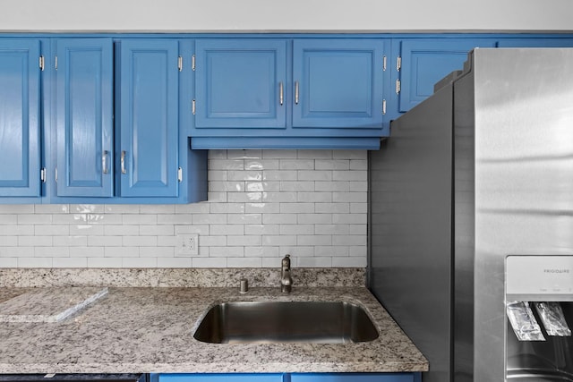 kitchen featuring tasteful backsplash, a sink, freestanding refrigerator, and blue cabinets