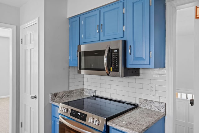 kitchen with appliances with stainless steel finishes, decorative backsplash, light stone countertops, and blue cabinets