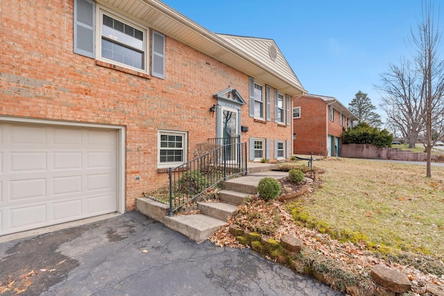 view of front of home featuring aphalt driveway, brick siding, an attached garage, and a front lawn