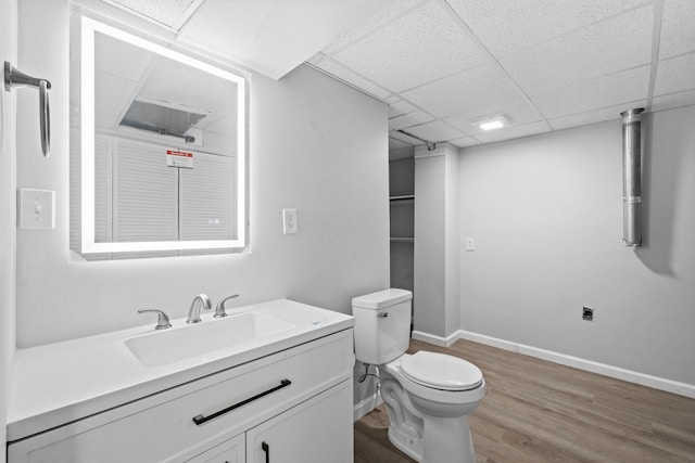 bathroom with a paneled ceiling, toilet, vanity, wood finished floors, and baseboards