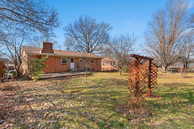 back of property featuring a chimney, fence, a lawn, and brick siding