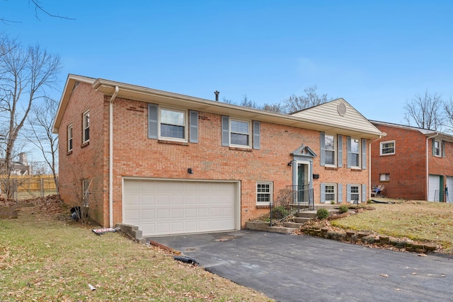 bi-level home featuring a garage, brick siding, a front yard, and aphalt driveway