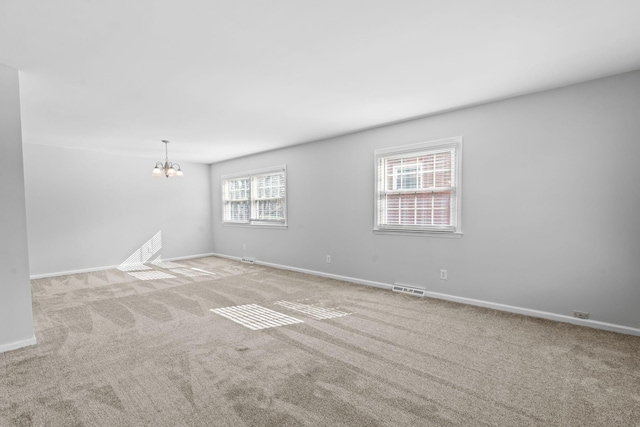 empty room featuring baseboards, carpet flooring, visible vents, and a notable chandelier