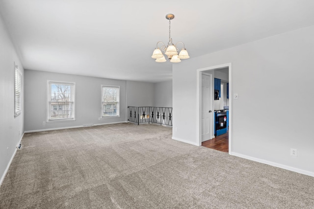 carpeted spare room with baseboards and a chandelier