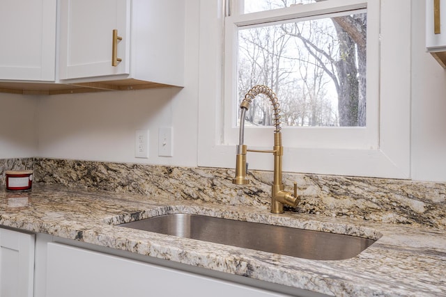 details with white cabinetry, light stone counters, and a sink