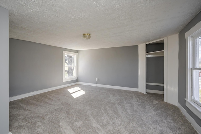 carpeted spare room featuring a textured ceiling and baseboards