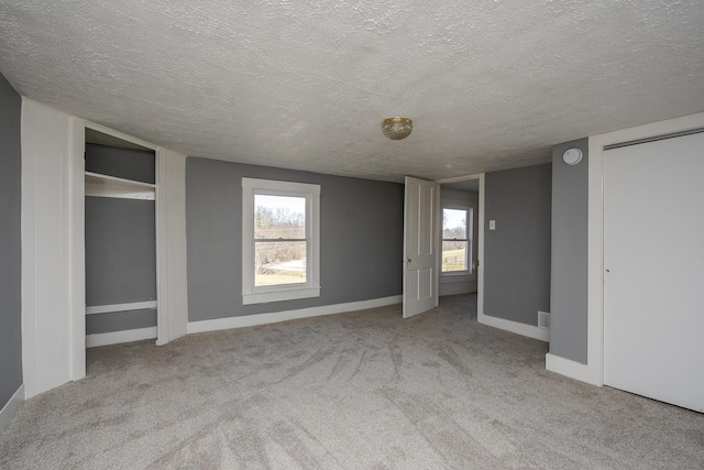 unfurnished bedroom featuring a textured ceiling, multiple windows, carpet, and baseboards