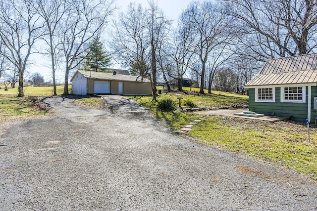 exterior space featuring driveway, a garage, metal roof, a standing seam roof, and an outdoor structure