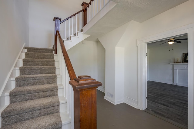 stairs with ceiling fan, a textured ceiling, and baseboards