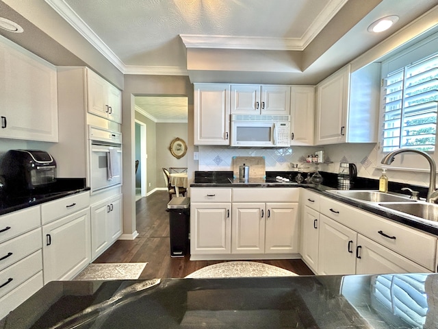 kitchen featuring dark countertops, white appliances, white cabinetry, and a sink