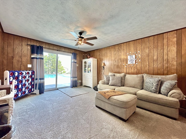 living area with wooden walls, a textured ceiling, a ceiling fan, and carpet flooring