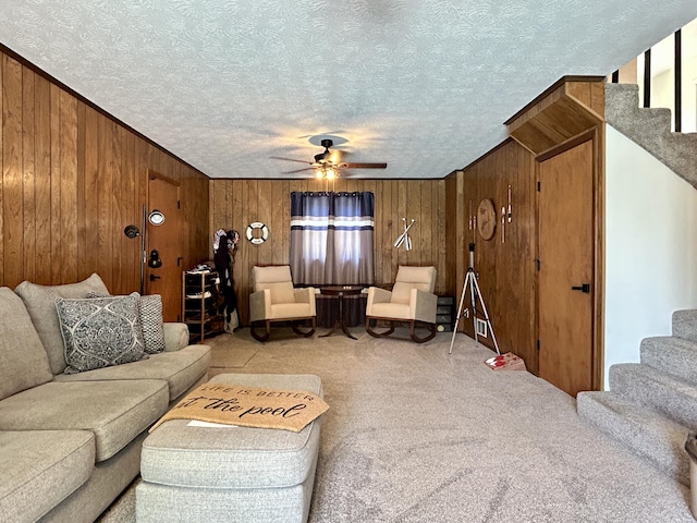 carpeted living room featuring a ceiling fan, wood walls, stairway, and a textured ceiling