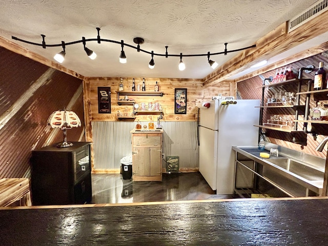 kitchen with wooden walls, visible vents, a textured ceiling, and freestanding refrigerator