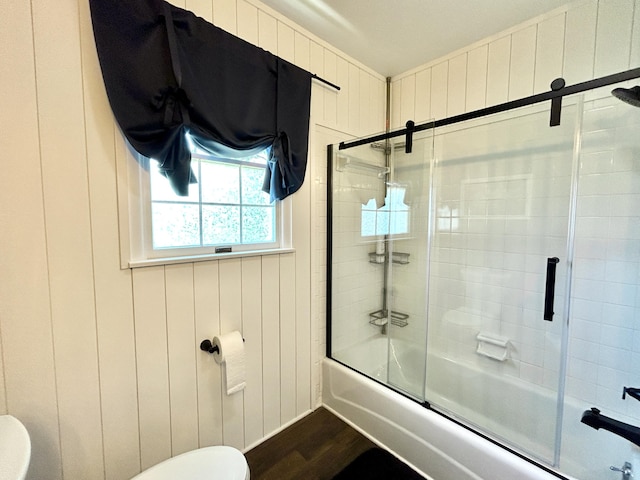 bathroom with toilet, wooden walls, bath / shower combo with glass door, and wood finished floors