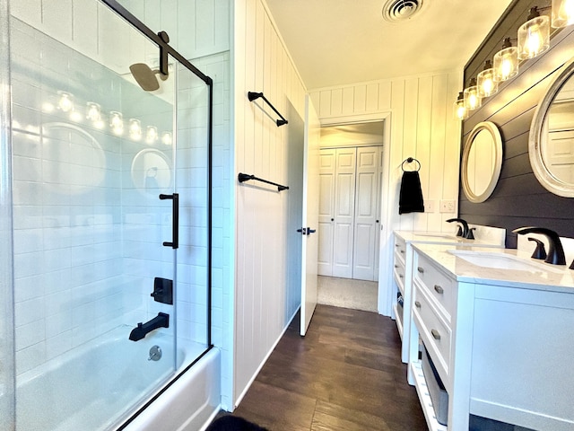 bathroom featuring shower / bath combination with glass door, double vanity, visible vents, a sink, and wood finished floors