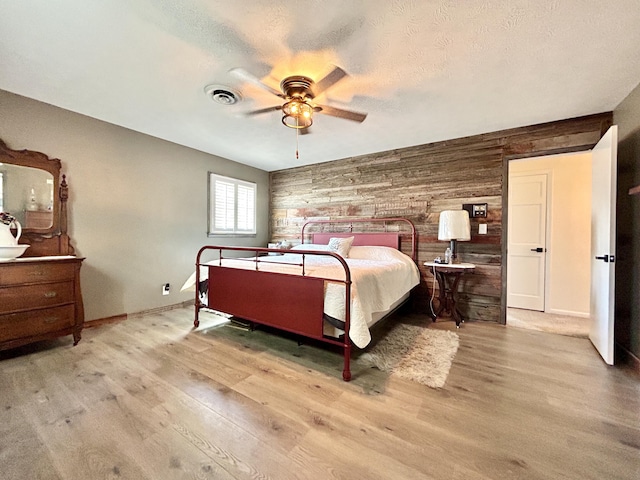 bedroom featuring wood walls, a textured ceiling, visible vents, and wood finished floors