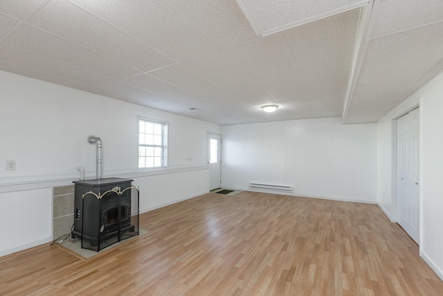 unfurnished living room with light wood-style floors, a wood stove, and baseboards