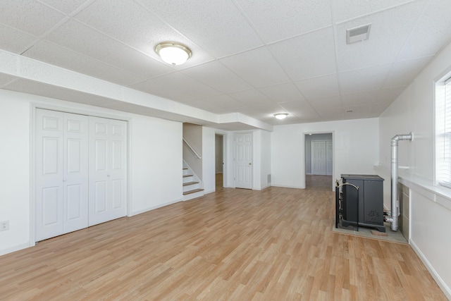 basement with light wood-type flooring, stairway, visible vents, and a wood stove