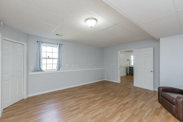 interior space featuring light wood finished floors, visible vents, baseboards, and a drop ceiling