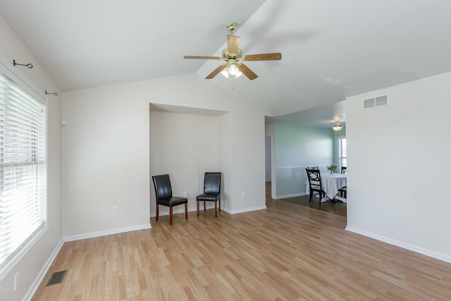 living area featuring light wood-type flooring, visible vents, lofted ceiling, and baseboards