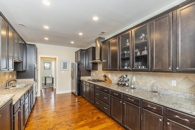 kitchen featuring dark brown cabinetry, appliances with stainless steel finishes, wall chimney range hood, and a sink