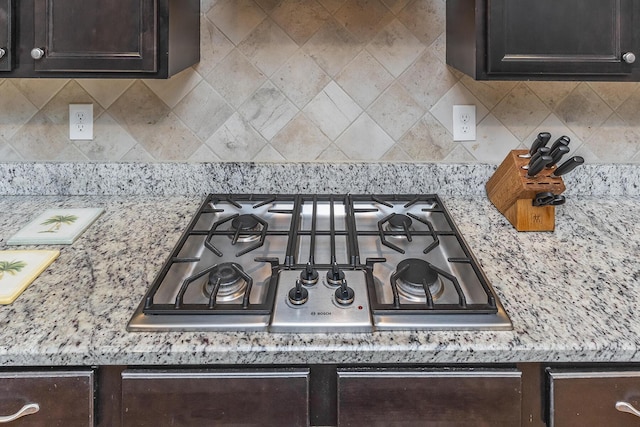 room details with decorative backsplash, dark brown cabinetry, stainless steel gas stovetop, and light stone countertops