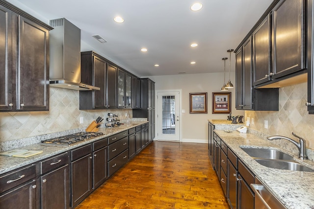 kitchen featuring light stone countertops, appliances with stainless steel finishes, dark wood-style floors, wall chimney exhaust hood, and a sink